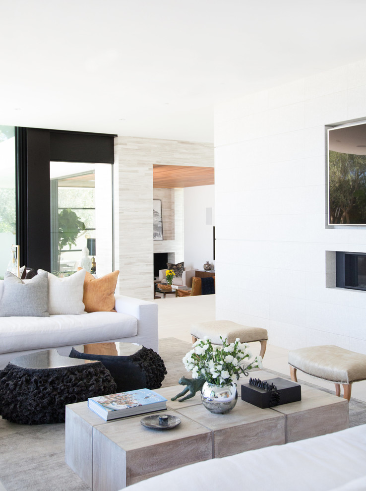 Идея дизайна: огромная парадная, открытая гостиная комната в современном стиле с белыми стенами, полом из известняка, двусторонним камином, фасадом камина из плитки и телевизором на стене
