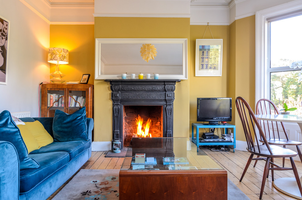 Eklektisches Wohnzimmer mit gelber Wandfarbe, braunem Holzboden, Kamin und freistehendem TV in Belfast