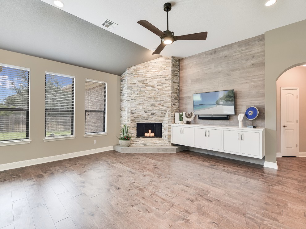 Mittelgroßes, Offenes Modernes Wohnzimmer mit beiger Wandfarbe, braunem Holzboden, Eckkamin, Kaminumrandung aus Stein, TV-Wand und braunem Boden in Austin