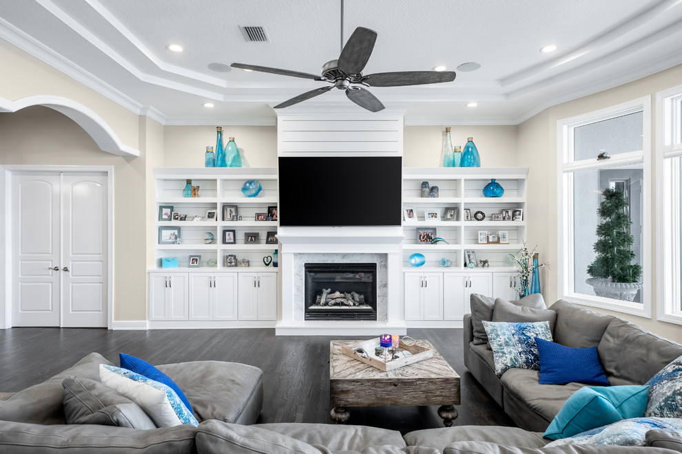 Large nautical open plan living room in Tampa with beige walls, dark hardwood flooring, a standard fireplace, a stone fireplace surround, a wall mounted tv and grey floors.