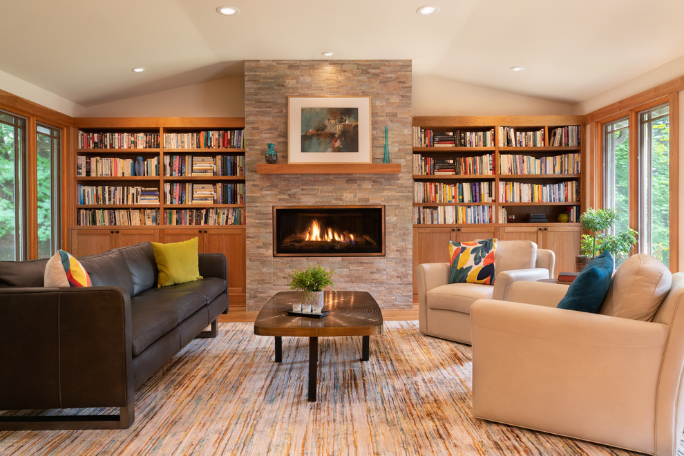 Idée de décoration pour un salon design avec une bibliothèque ou un coin lecture, un mur beige, un sol en bois brun, une cheminée ribbon et un manteau de cheminée en pierre.