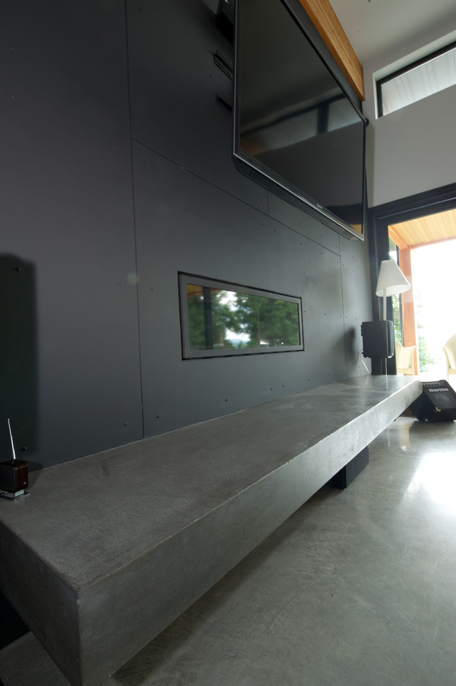 Стильный дизайн: огромная открытая гостиная комната в стиле модернизм с черными стенами, бетонным полом и телевизором на стене - последний тренд