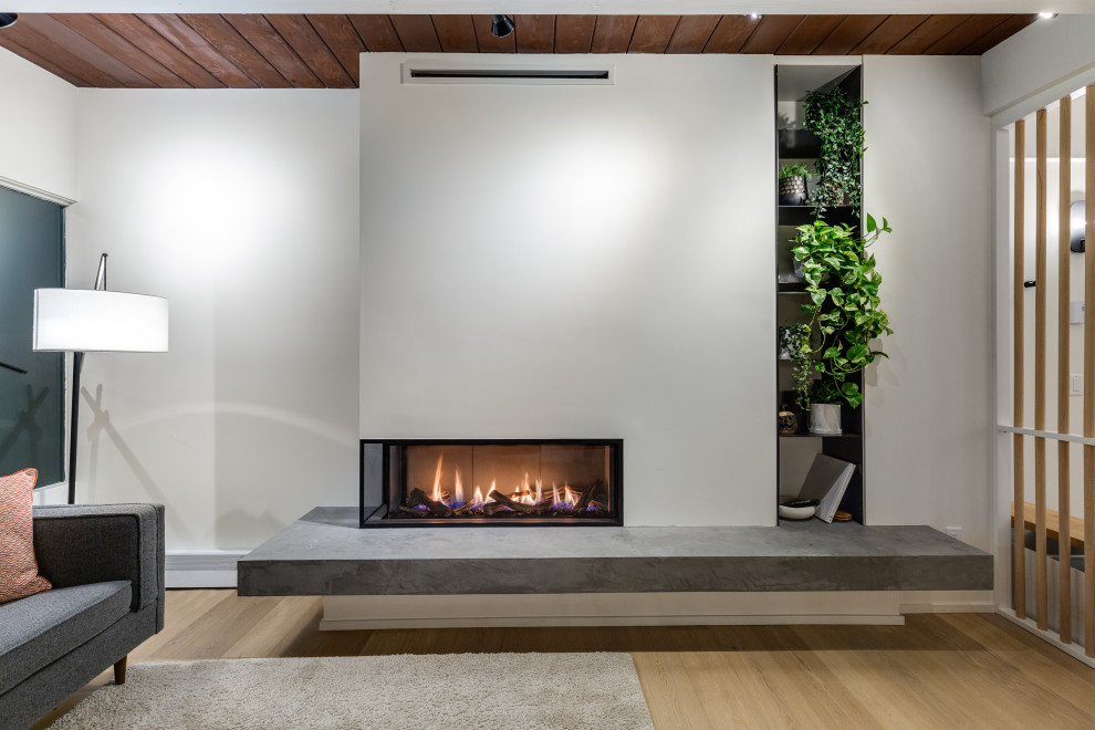 Photo of a medium sized retro open plan living room in Vancouver with white walls, light hardwood flooring, a corner fireplace and a concrete fireplace surround.