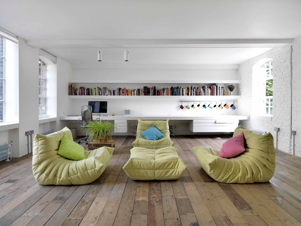 Idées déco pour un salon industriel ouvert avec une bibliothèque ou un coin lecture, un mur blanc et un sol en bois brun.