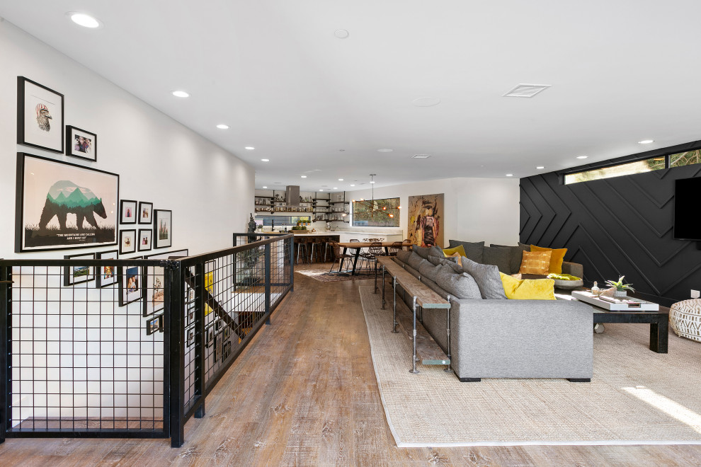 Imagen de salón abierto urbano con paredes grises, suelo de madera en tonos medios, televisor colgado en la pared, suelo marrón y panelado