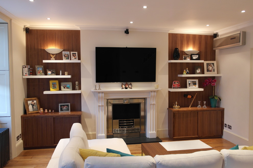 Mid-sized trendy formal and enclosed medium tone wood floor living room photo in London with white walls, a standard fireplace, a plaster fireplace and a wall-mounted tv