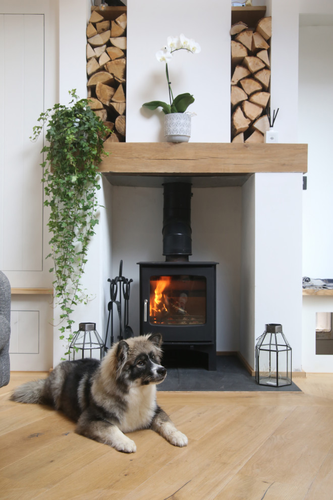 This is an example of a small scandi open plan living room in Hampshire with white walls, light hardwood flooring, a wood burning stove, a plastered fireplace surround and a wall mounted tv.