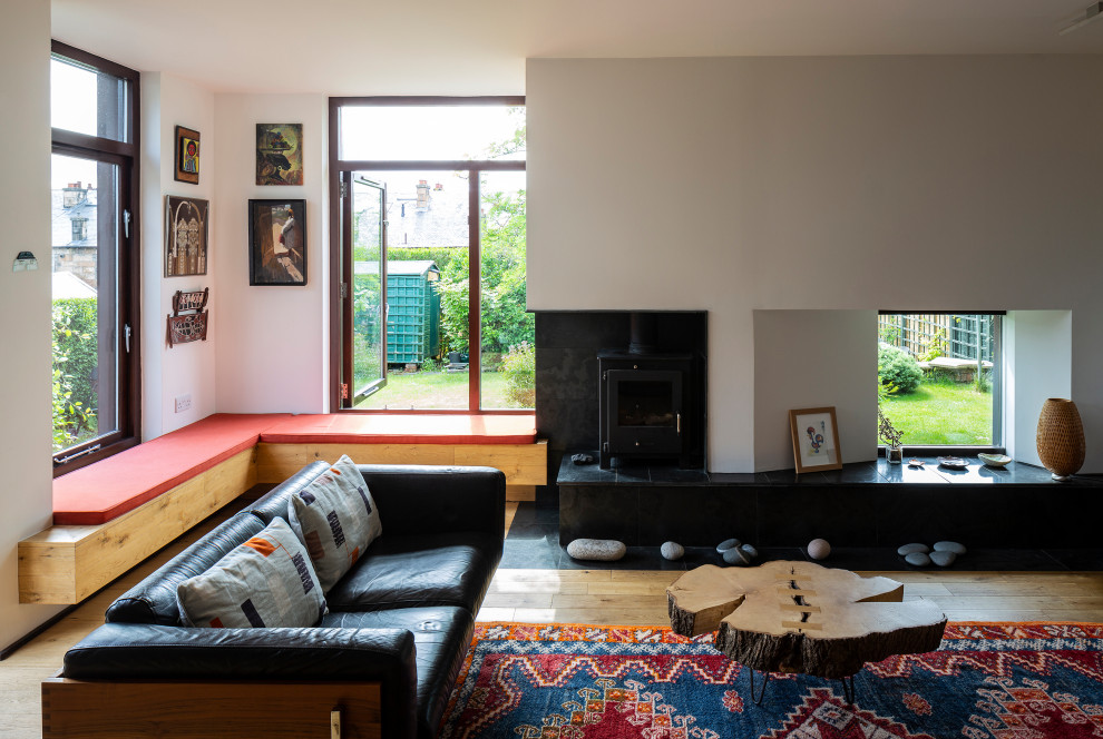 На фото: открытая гостиная комната среднего размера в современном стиле с светлым паркетным полом, печью-буржуйкой и фасадом камина из камня