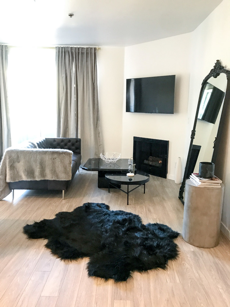 Kleines, Abgetrenntes Modernes Wohnzimmer mit weißer Wandfarbe, hellem Holzboden, Eckkamin, Kaminumrandung aus Metall, TV-Wand und braunem Boden in Los Angeles