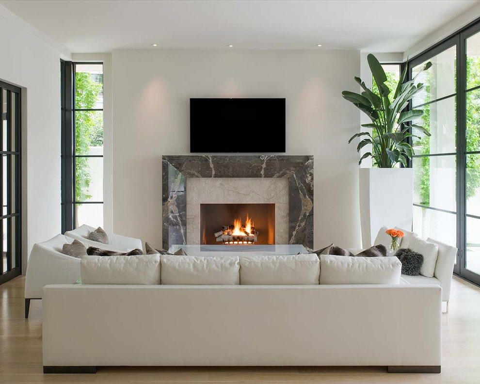 Idée de décoration pour un salon design de taille moyenne et ouvert avec un mur blanc, une cheminée standard, un manteau de cheminée en pierre, un téléviseur fixé au mur, un sol beige et parquet clair.