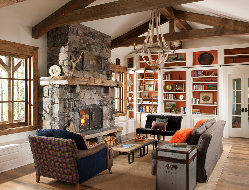 Aménagement d'un salon montagne avec une bibliothèque ou un coin lecture, un mur blanc, un sol en bois brun, une cheminée standard et un manteau de cheminée en pierre.