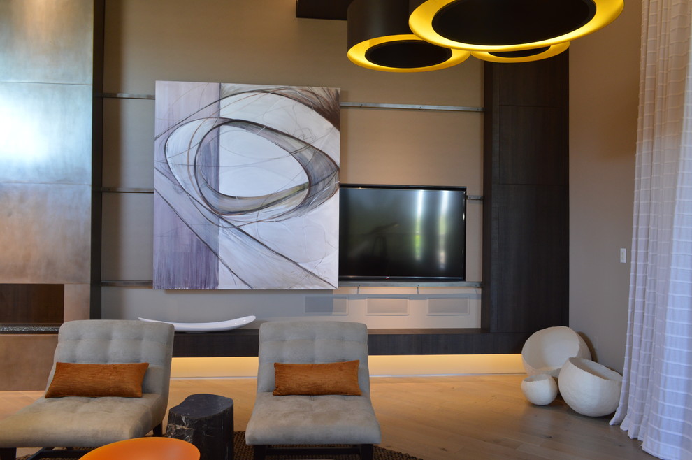 Modelo de salón abierto contemporáneo de tamaño medio con paredes beige, suelo de madera clara, chimenea de doble cara, marco de chimenea de metal y televisor retractable