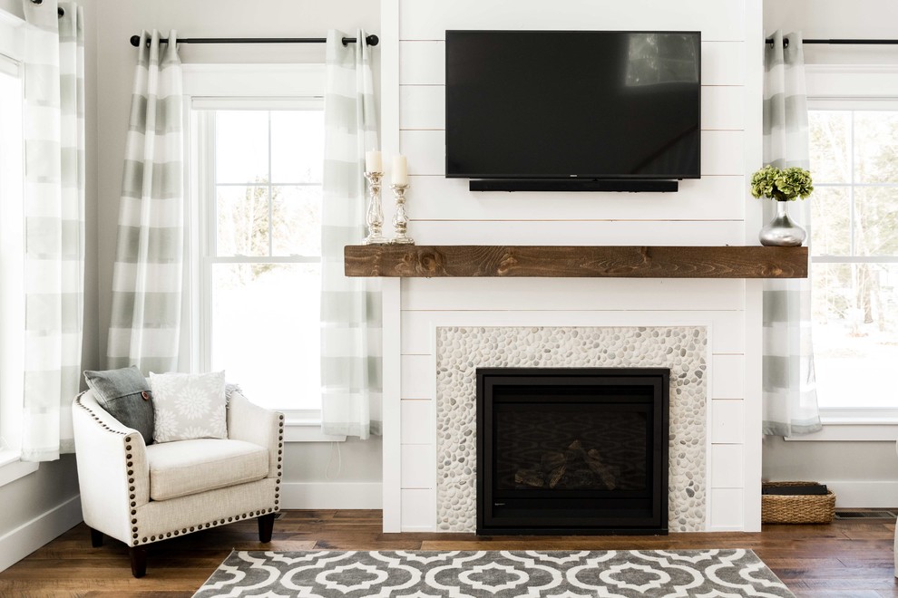 Photo of a large country open plan living room in Portland Maine with grey walls, medium hardwood flooring, a standard fireplace, a stone fireplace surround, a wall mounted tv and brown floors.