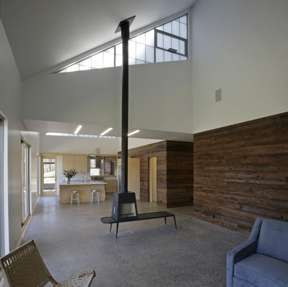 Modelo de salón abierto moderno de tamaño medio con suelo de cemento, estufa de leña y paredes blancas