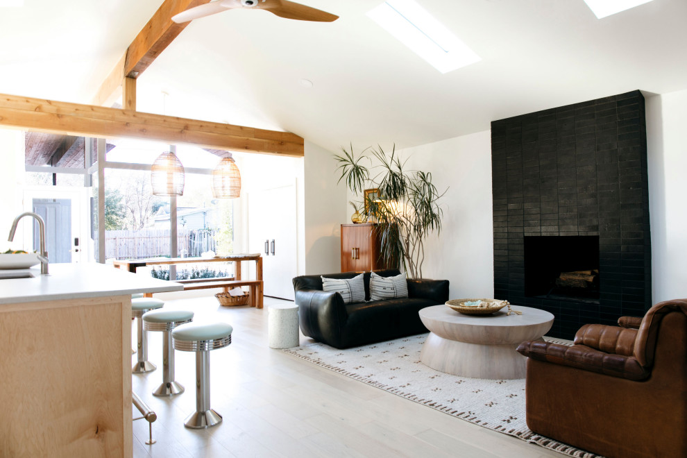 Offenes Modernes Wohnzimmer mit weißer Wandfarbe, hellem Holzboden, Kamin, gefliester Kaminumrandung, beigem Boden und gewölbter Decke in Austin