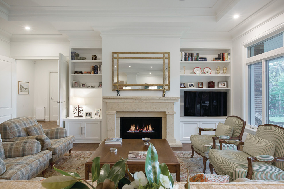 Aménagement d'un grand salon classique fermé avec un mur blanc, un manteau de cheminée en pierre, un sol en bois brun, une cheminée standard et un téléviseur encastré.