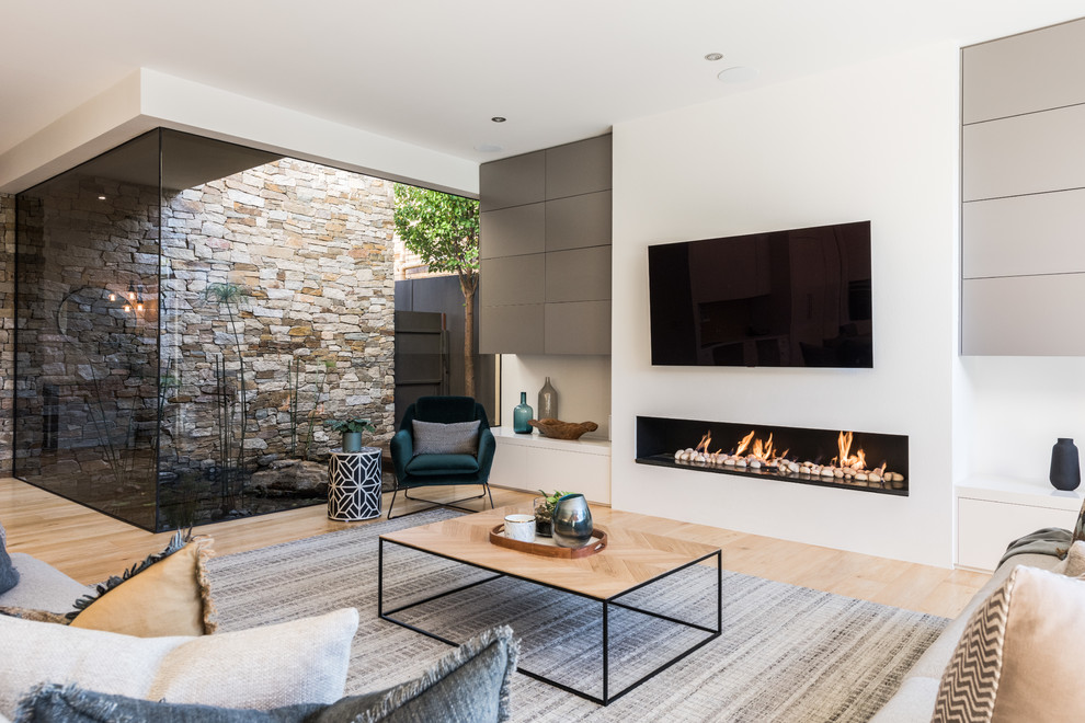 This is an example of a contemporary grey and teal open plan living room in Melbourne with white walls, light hardwood flooring, a ribbon fireplace, a wall mounted tv and beige floors.
