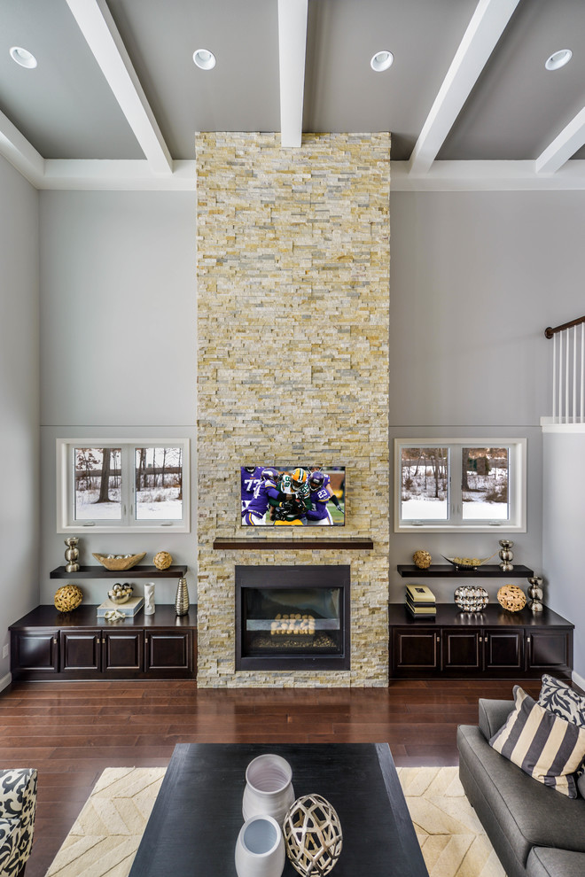 На фото: большая открытая гостиная комната в стиле модернизм с серыми стенами, темным паркетным полом, стандартным камином, фасадом камина из камня и телевизором на стене