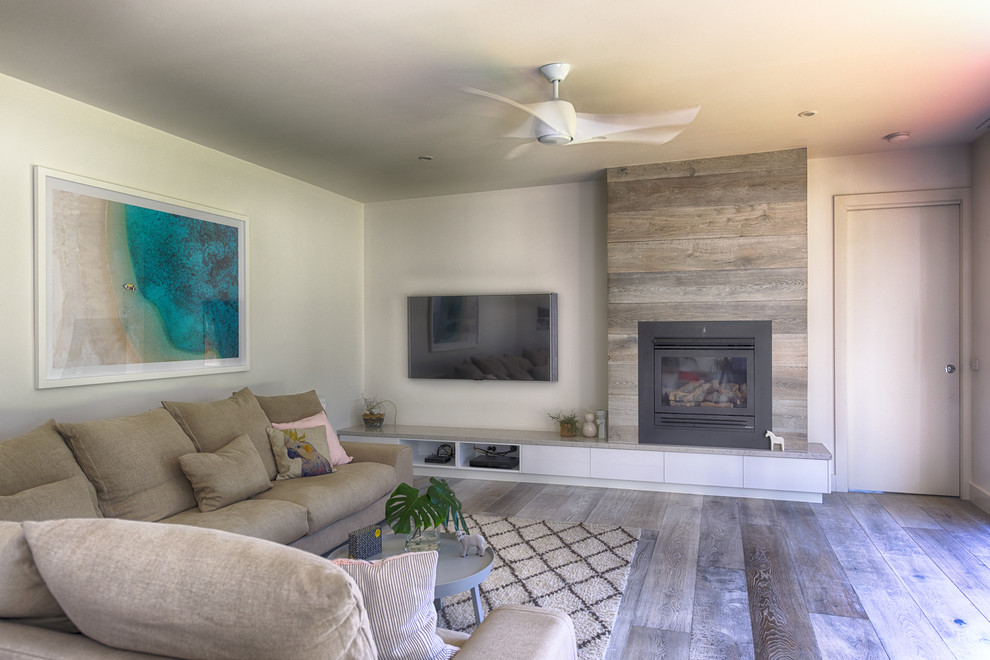 Cette image montre un grand salon design ouvert avec un mur blanc, parquet clair, une cheminée standard, un téléviseur fixé au mur et un sol gris.
