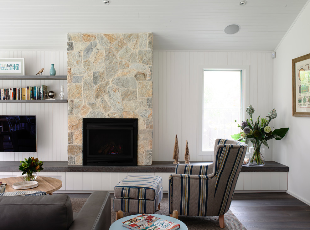 На фото: открытая гостиная комната в морском стиле с белыми стенами, фасадом камина из камня, телевизором на стене и стандартным камином с
