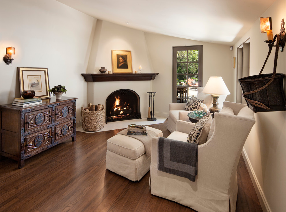 Mediterranean living room in Santa Barbara with a corner fireplace, white walls and feature lighting.