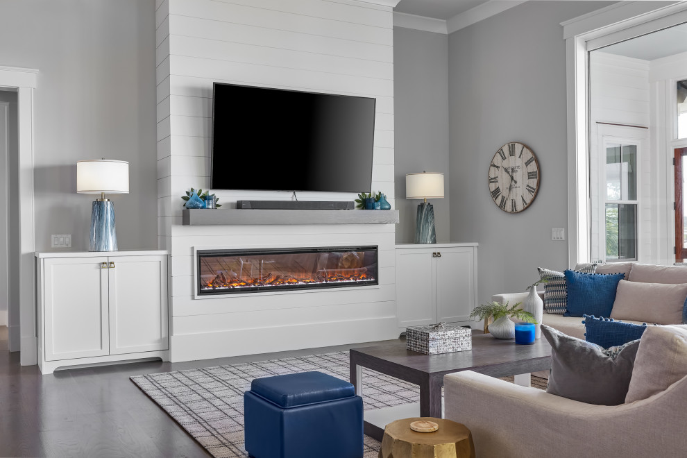 Источник вдохновения для домашнего уюта: большая открытая гостиная комната в морском стиле с серыми стенами, темным паркетным полом, фасадом камина из вагонки, телевизором на стене и коричневым полом