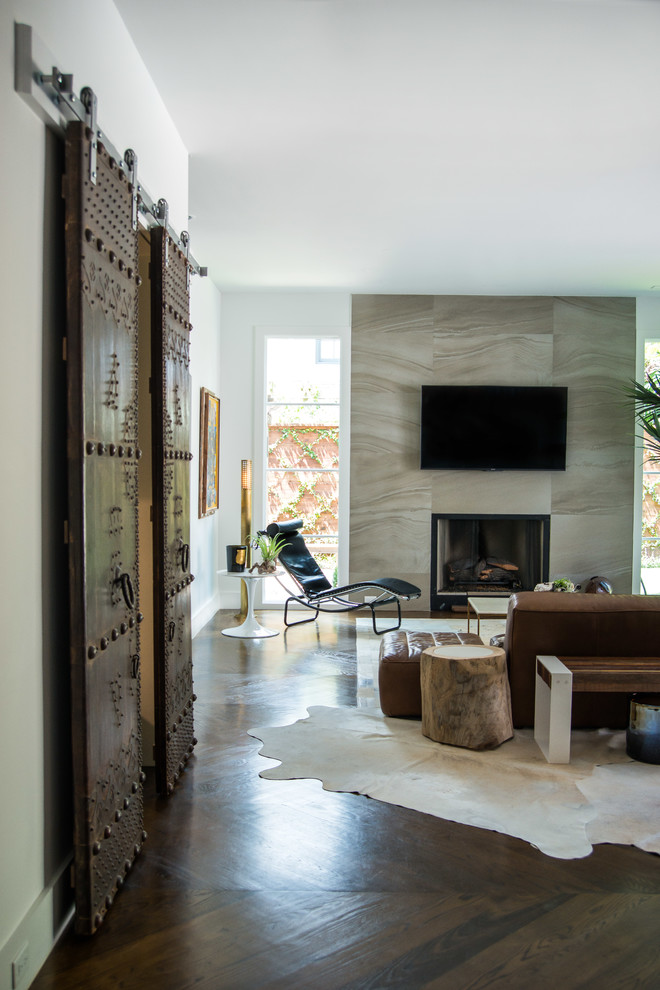 На фото: большая открытая гостиная комната в стиле неоклассика (современная классика) с белыми стенами, паркетным полом среднего тона, стандартным камином, фасадом камина из камня, телевизором на стене и коричневым полом