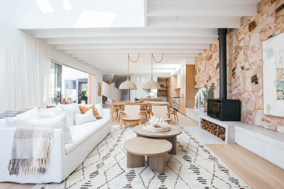 Inspiration for a beach style living room in Central Coast with white walls, light hardwood flooring, a wood burning stove, beige floors and exposed beams.