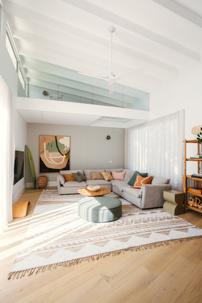 Diseño de salón abierto y abovedado costero con paredes blancas, suelo de madera clara, suelo beige y vigas vistas
