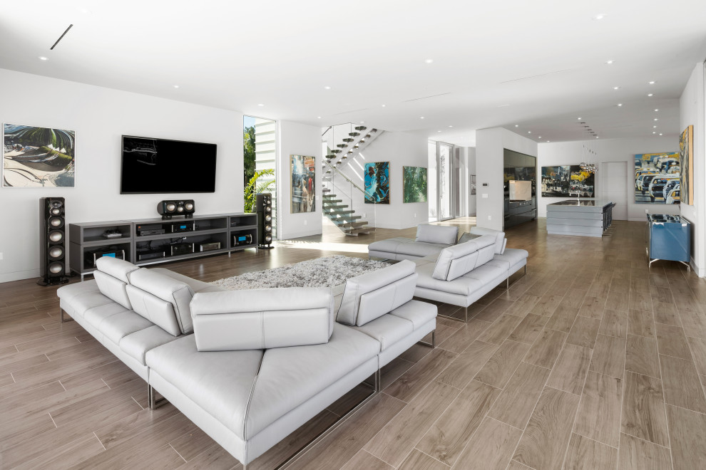 Diseño de salón abierto minimalista extra grande con paredes blancas, suelo de baldosas de porcelana, televisor colgado en la pared y suelo marrón