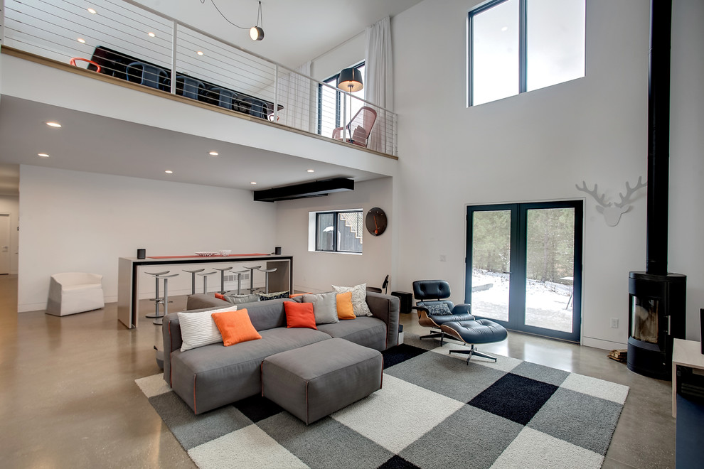 На фото: двухуровневая гостиная комната в стиле модернизм с белыми стенами, бетонным полом, печью-буржуйкой и телевизором на стене с