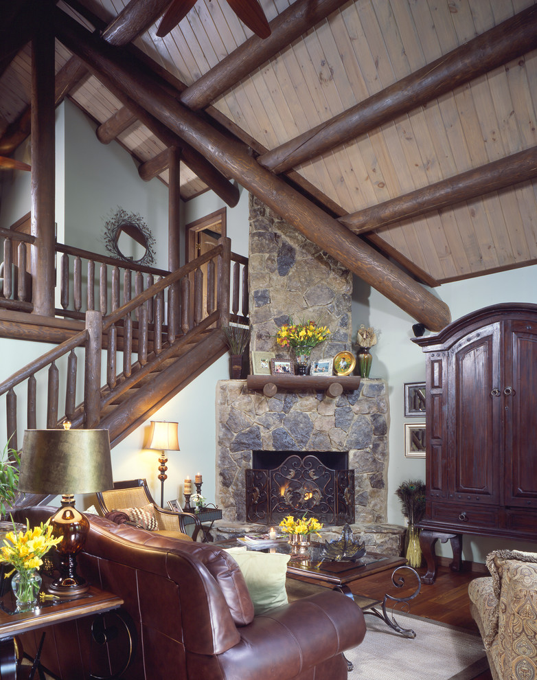 Idée de décoration pour un salon chalet de taille moyenne et ouvert avec un mur gris, un sol en bois brun, une cheminée d'angle et un manteau de cheminée en pierre.