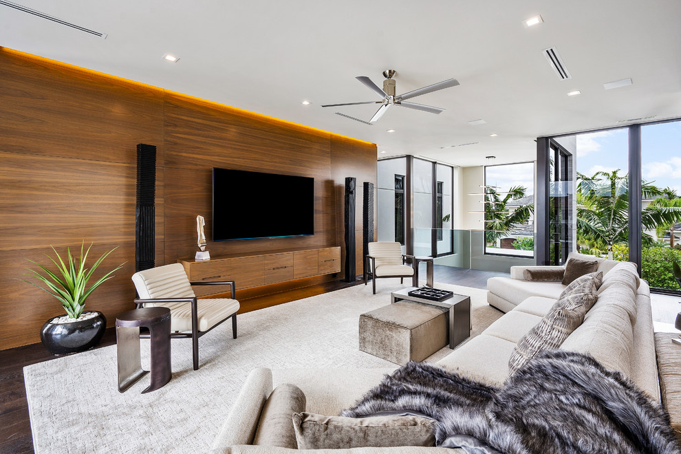 Modelo de salón abierto contemporáneo grande con paredes marrones, televisor colgado en la pared, suelo marrón y suelo de madera oscura