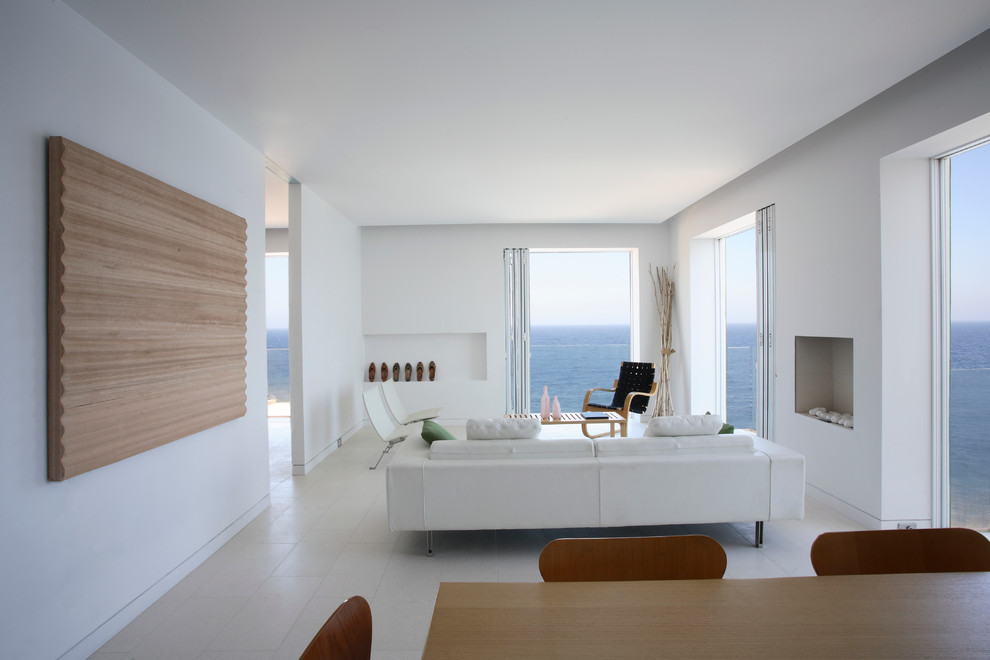Cette image montre un petit salon minimaliste ouvert avec un mur blanc, une cheminée standard, aucun téléviseur, un sol en calcaire, un sol blanc et un manteau de cheminée en pierre.