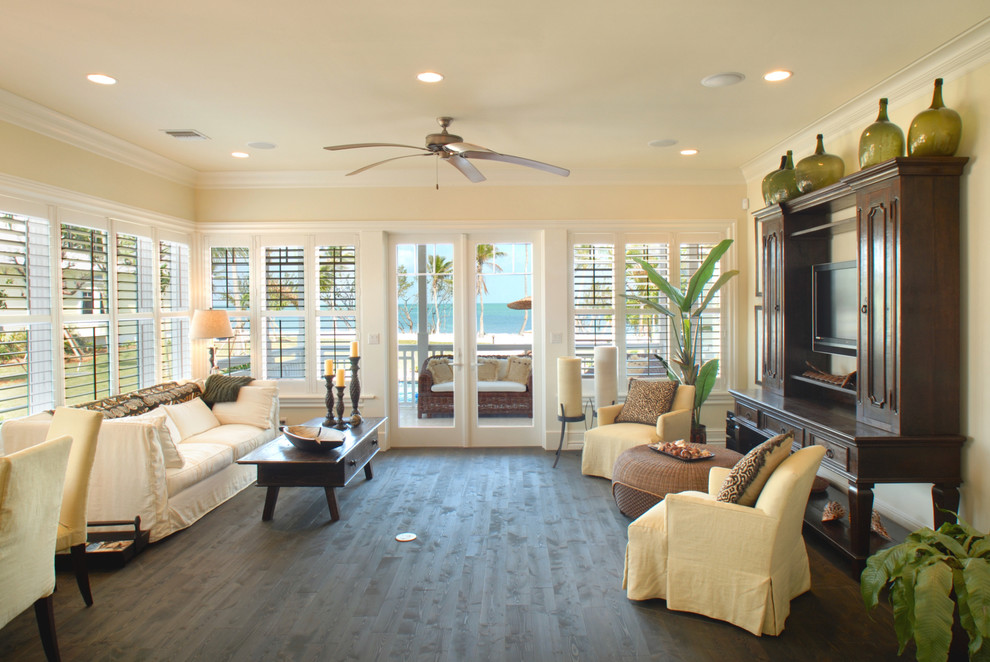 Example of a large island style open concept dark wood floor and brown floor living room design in Miami with beige walls and a concealed tv