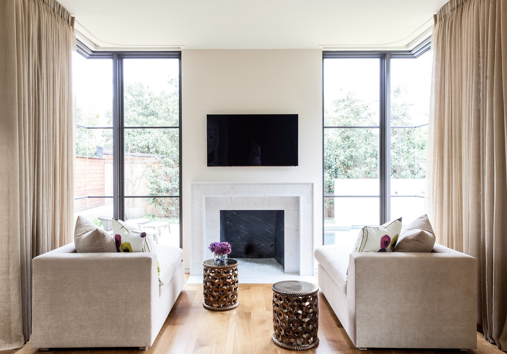 Esempio di un soggiorno minimal con pareti beige, pavimento in legno massello medio e TV a parete