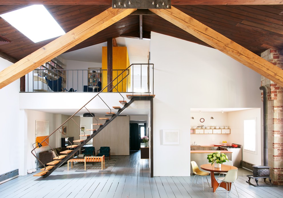 Exemple d'un salon mansardé ou avec mezzanine industriel avec un mur blanc, un sol gris, parquet peint, un poêle à bois et un escalier.