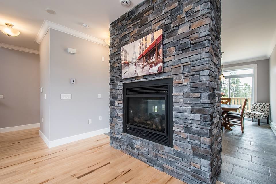 他の地域にあるトラディショナルスタイルのおしゃれなLDK (グレーの壁、淡色無垢フローリング、両方向型暖炉、石材の暖炉まわり、ベージュの床) の写真