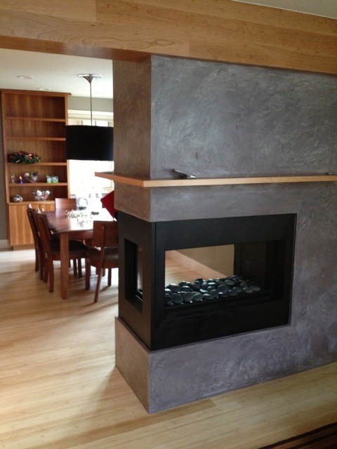 Foto de salón abierto actual de tamaño medio con paredes marrones, suelo de madera clara, chimenea de doble cara y marco de chimenea de hormigón