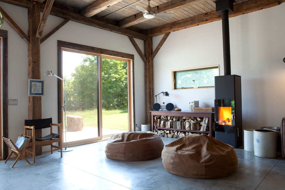 Example of a large mountain style open concept concrete floor and gray floor living room design in New York with a wood stove, white walls, a metal fireplace and no tv