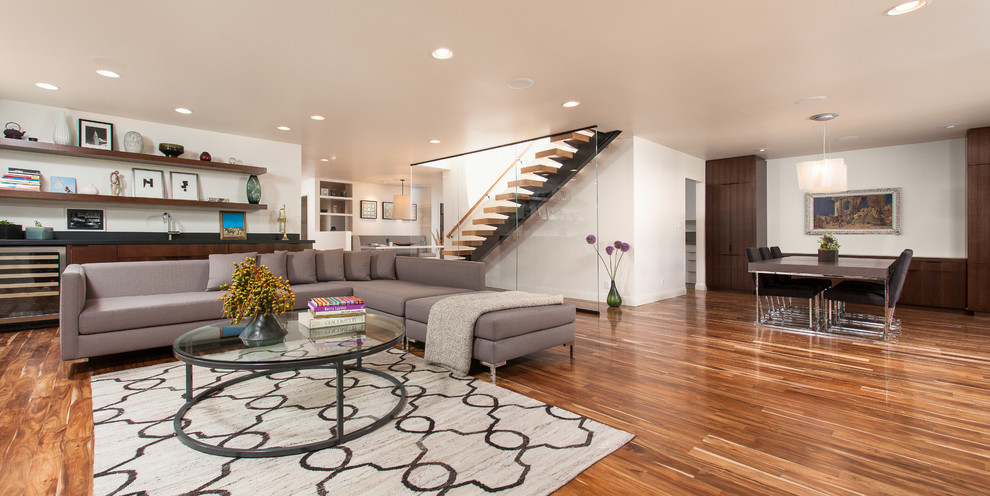 Offenes, Großes Modernes Wohnzimmer mit weißer Wandfarbe, braunem Holzboden, Eckkamin, Kaminumrandung aus Stein und braunem Boden in Los Angeles