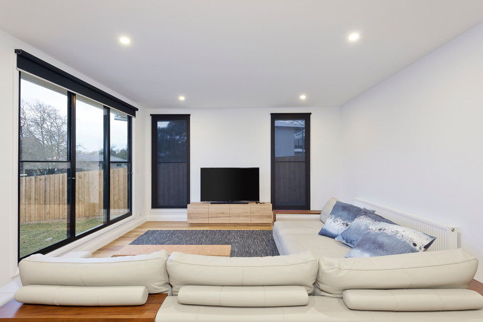 This is an example of a medium sized contemporary open plan living room in Melbourne with white walls, light hardwood flooring and a freestanding tv.
