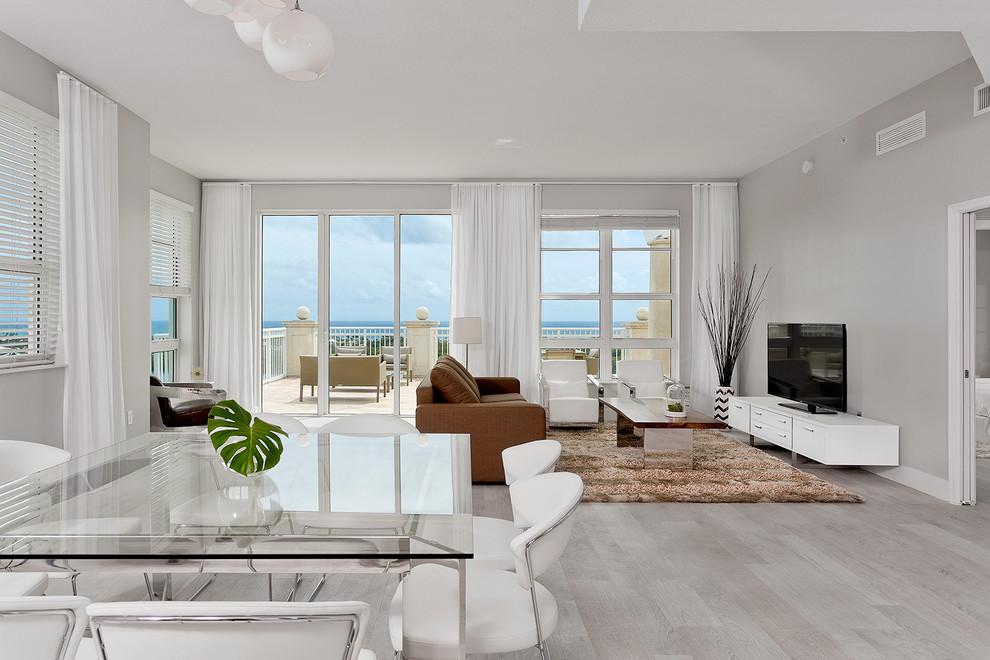 Offenes Modernes Wohnzimmer ohne Kamin mit hellem Holzboden, grauer Wandfarbe, freistehendem TV und grauem Boden in Miami