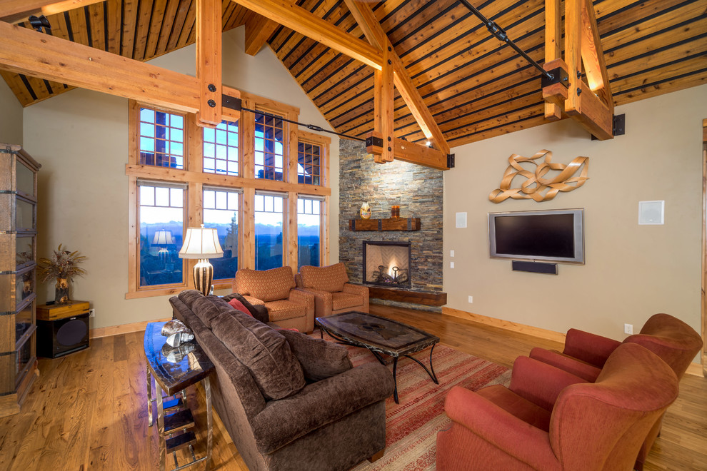 На фото: гостиная комната в стиле рустика с бежевыми стенами, угловым камином, телевизором на стене и коричневым диваном