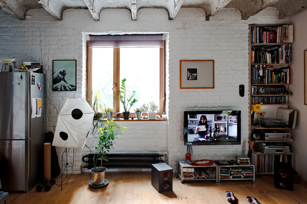 Foto på ett industriellt vardagsrum, med vita väggar, mellanmörkt trägolv och en väggmonterad TV