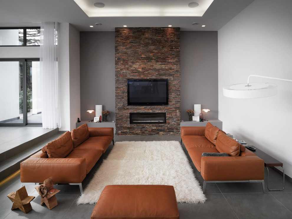 Diseño de salón abierto contemporáneo de tamaño medio con paredes grises, todas las chimeneas, marco de chimenea de piedra, televisor colgado en la pared, suelo de pizarra y suelo gris