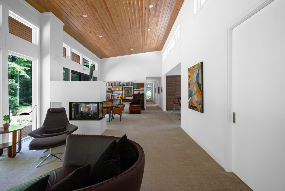 Immagine di un soggiorno moderno di medie dimensioni e aperto con libreria, pareti bianche, moquette, camino bifacciale, cornice del camino piastrellata, pavimento beige e soffitto a volta