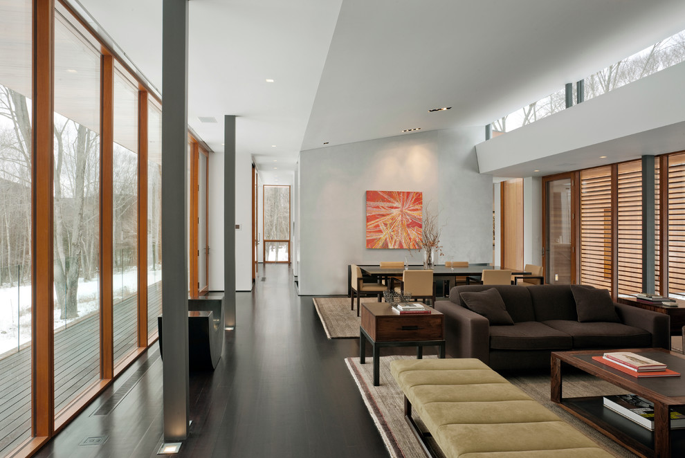 На фото: открытая гостиная комната в современном стиле с белыми стенами, темным паркетным полом и коричневым диваном
