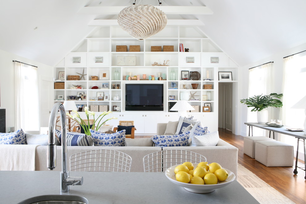 Modelo de salón abierto marinero con paredes blancas, suelo de madera en tonos medios y televisor colgado en la pared