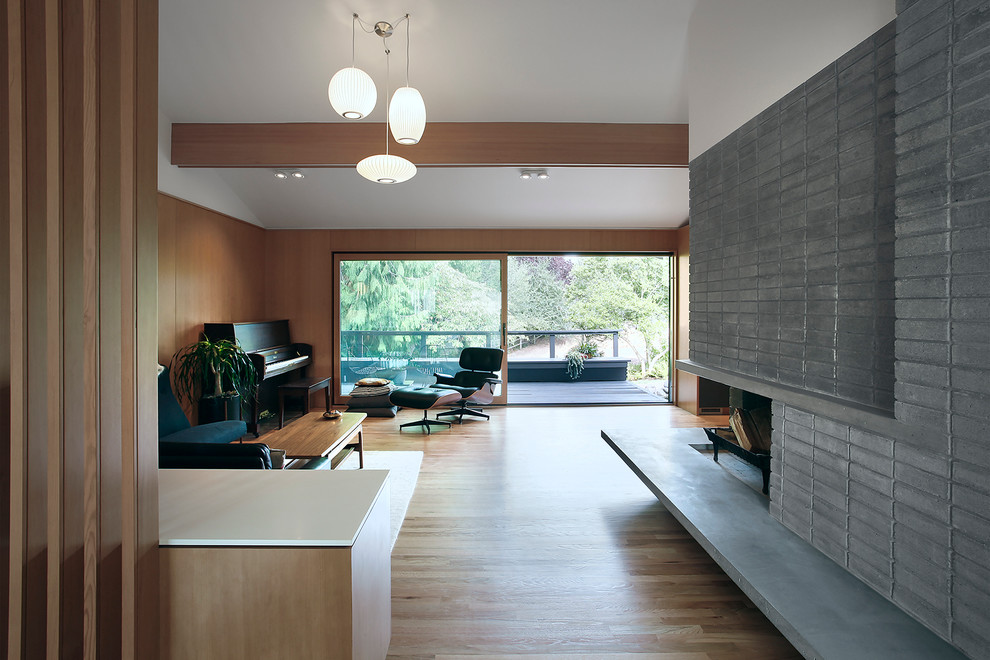 This is an example of a large midcentury open plan living room in Seattle with a music area, brown walls, light hardwood flooring, a two-sided fireplace, a stone fireplace surround and no tv.